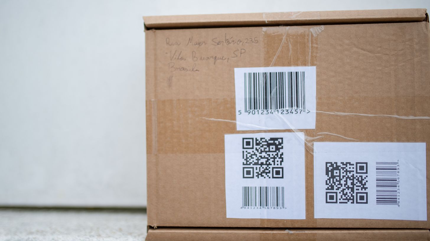 2D barcode labels printed on a cardboard carton next to a traditional linear barcode