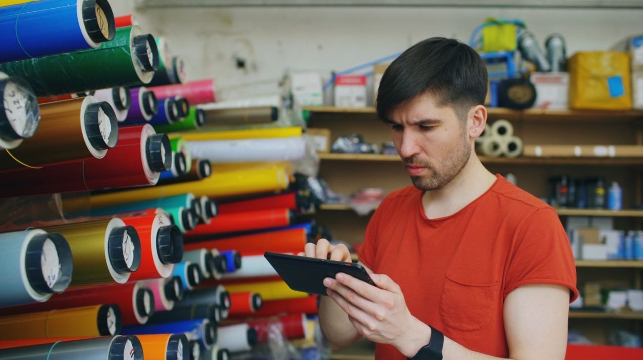Operator with a tablet beside colourful label rolls in a print shop
